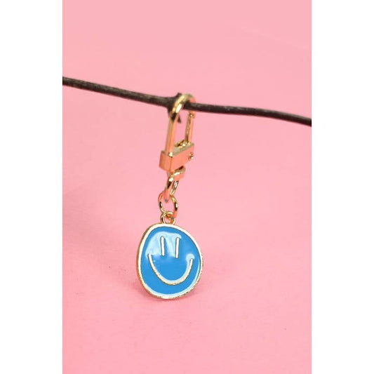 A sky blue keychain with a smiling face design, attached to a gold-colored metal ring, displayed against a pink background.