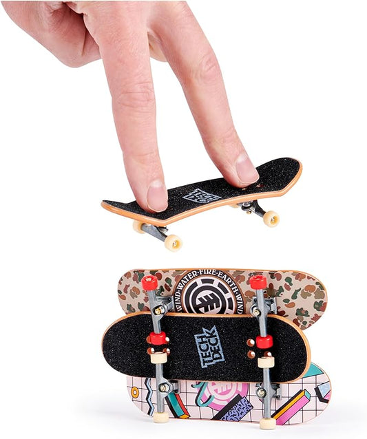 A hand holding a fingerboard from the Tech Deck Ultra DLX Pack, with three additional fingerboards featuring various skate graphics displayed below.
