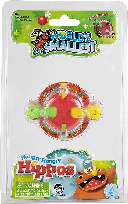 The product is a small, hand-sized version of the game 'Hungry Hungry Hippos'. It is packaged in a clear plastic blister pack, showing a colorful hippo-shaped game piece with red and green elements, against a green and white themed background card.