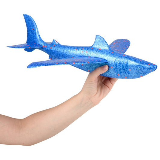 A hand holding a blue and multicolor shark-shaped glider toy with a wingspan.