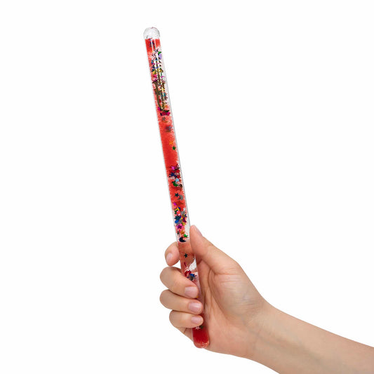 A hand holding a red wand-shaped toy filled with glitter and confetti, against a white background.