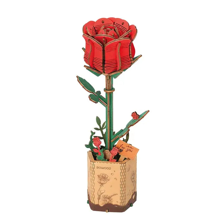 A completed 3D wooden puzzle model of a red rose with green leaves, mounted on a brown base that resembles a paper with a watermark 'ROBOTIME'.