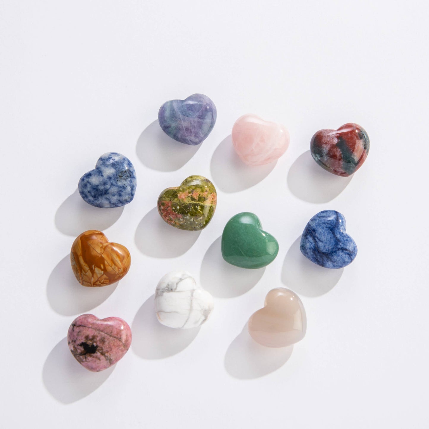 A collection of polished mineral hearts in various colors arranged on a white surface.