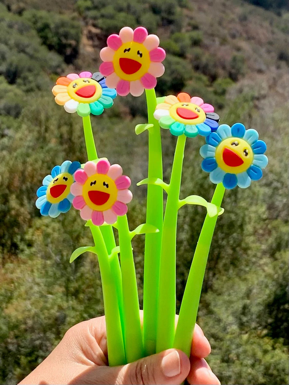 A set of colorful gel pens with flower designs held in a person's hand.