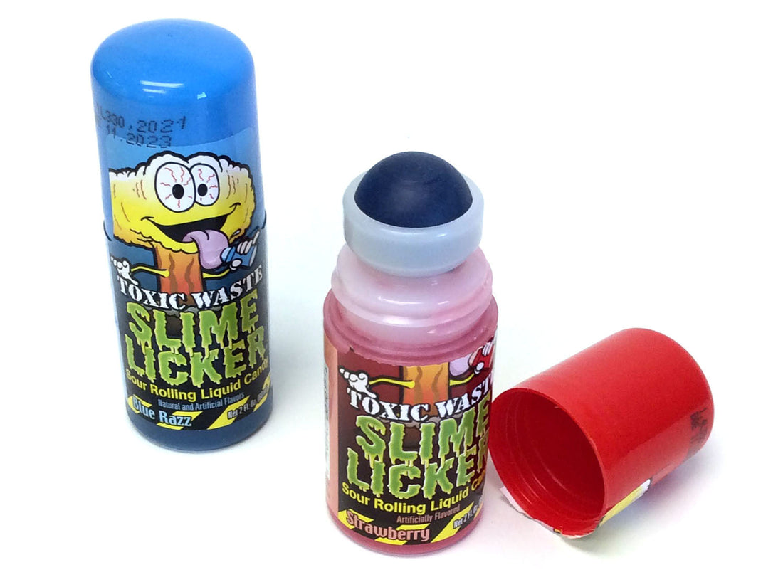 The image shows a container of Toxic Waste Slime Lickers candy, with its lid off revealing a red liquid inside. The container has a cartoonish design with the product name and flavor, Blue Razz, visible.